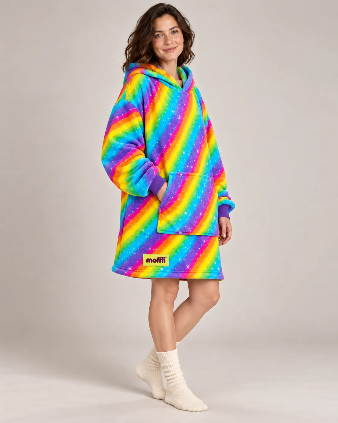Woman sitting on the sofa wrapped in the Rainbow Moffli with hood up and legs tucked in