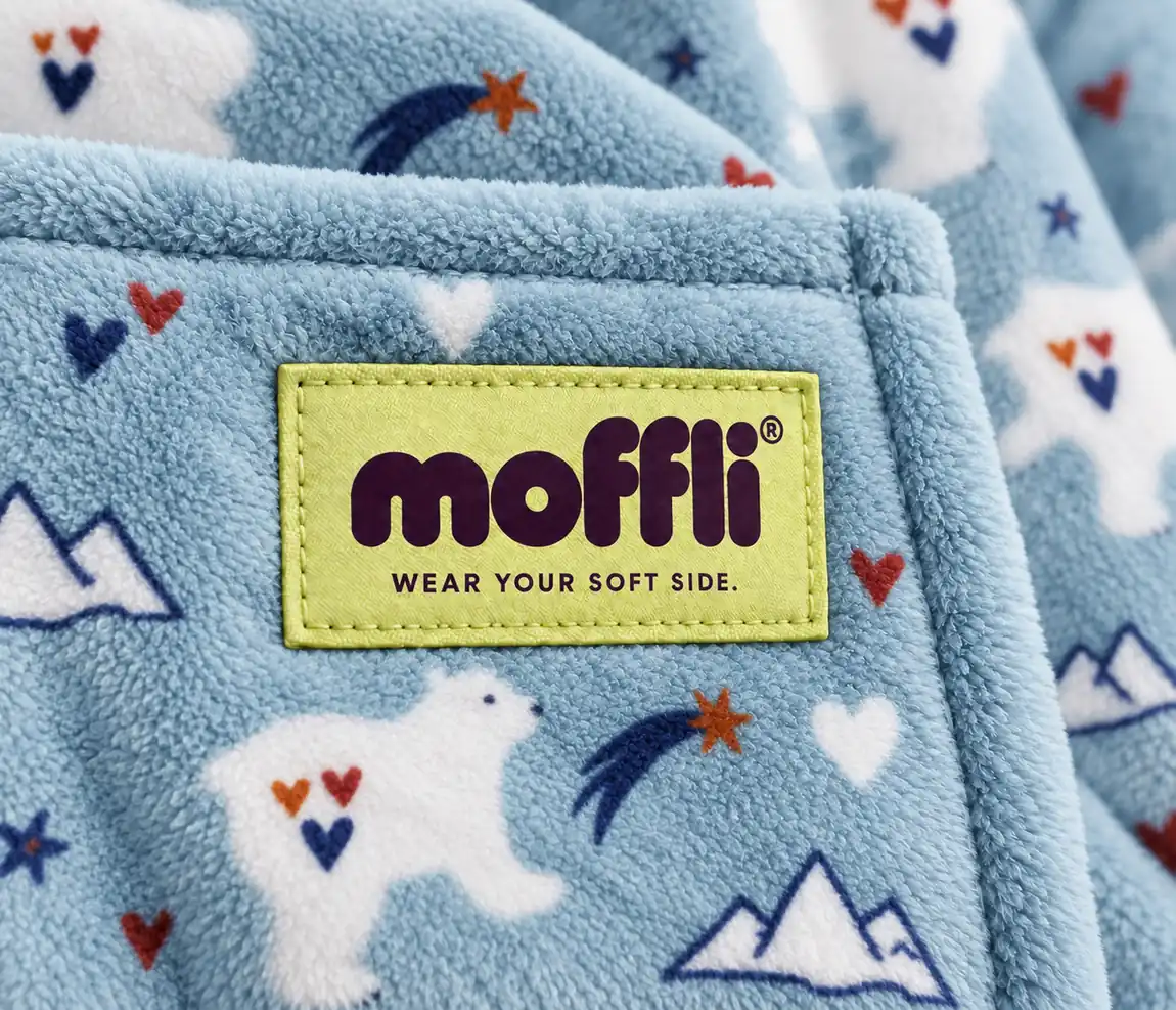 Close-up of the blue fleece of the Polar Bear Kids Moffli with bear, heart, star and mountain print and Moffli "Wear your soft side" label