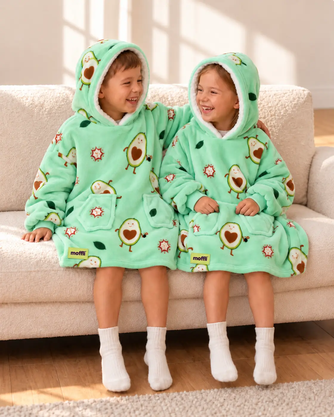 Boy and girl sitting on the sofa wearing the Avocado Love Kids Moffli and hood up