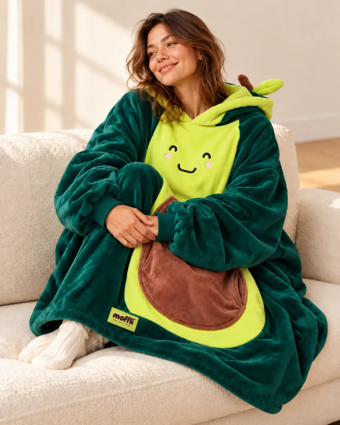 Woman sitting on the sofa wrapped in the Avocado Moffli, with smiling face and pit pocket