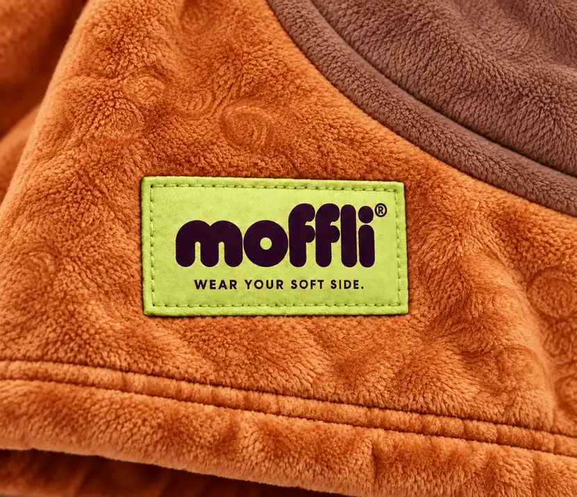 Close-up of the orange fleece of the Capybara Kids Moffli with brown panel and Moffli "Wear your soft side" label