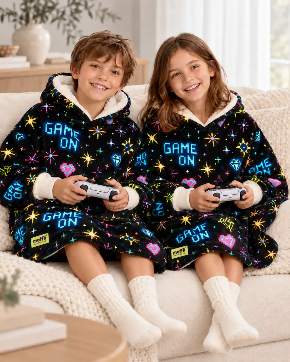 Boy and girl sitting on the sofa wearing the Game On Moffli while playing with controllers
