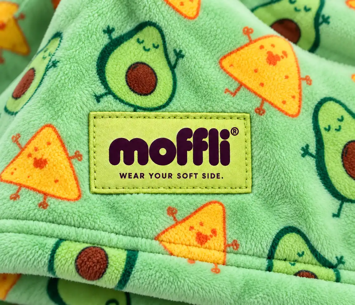 Macro del tessuto verde con fantasia di avocado e nachos ed etichetta Moffli "Wear your soft side."