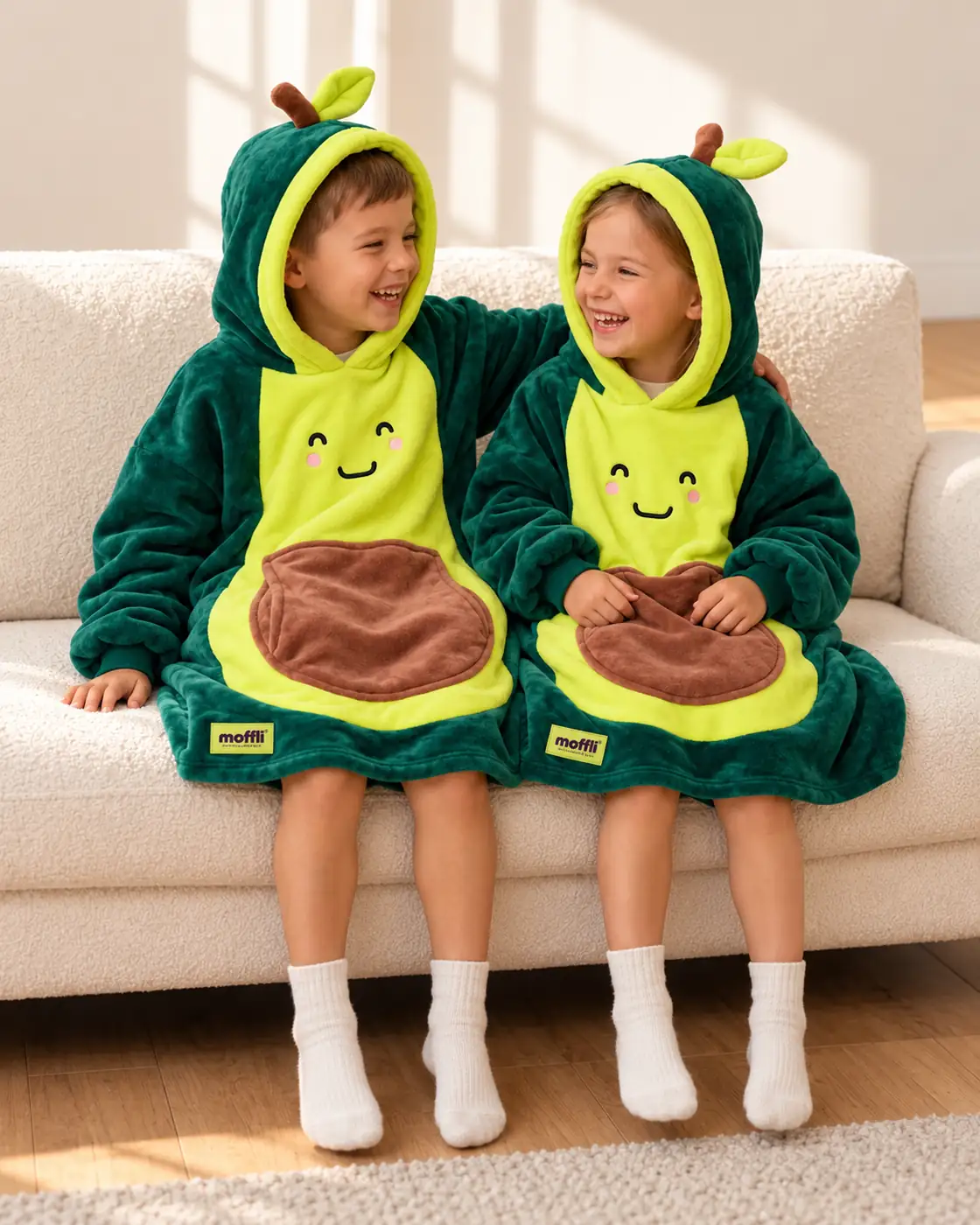 Boy and girl sitting on the sofa wearing the Avocado Kids Moffli, hoods up